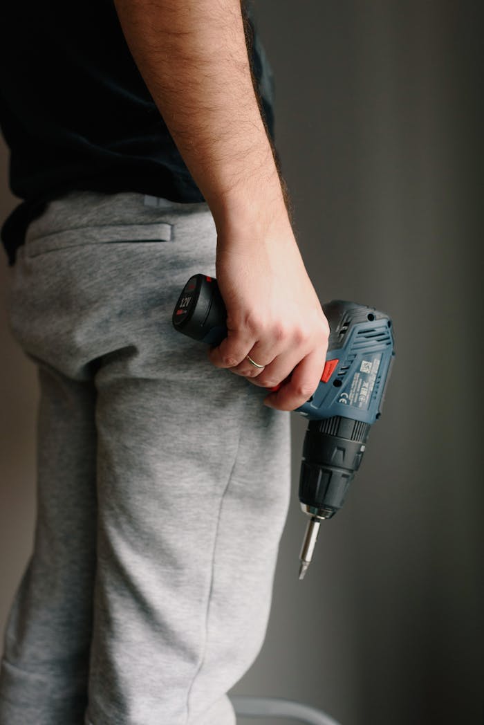 our-story A man holds a cordless drill, ready for work, against a neutral indoor background.