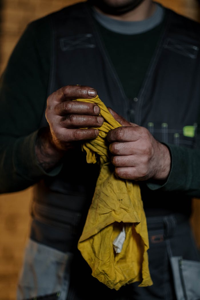 Crop anonymous male mechanic in uniform wiping greased hands while standing in repair workshop